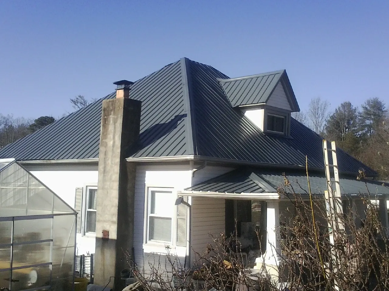 Dark blue standing seam metal roof on a white farmhouse with dormer — Slate & Tile Roof Repair by Roofing Brothers in Cobalt