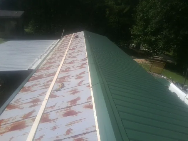 Old rusted panels beside newly installed green metal roofing — Wind Damage Roof Repair by Roofing Brothers in Cobalt