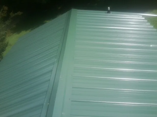 New green metal panels meeting at the ridge of a roof — Flat Roof Repair work by our crew in Cobalt
