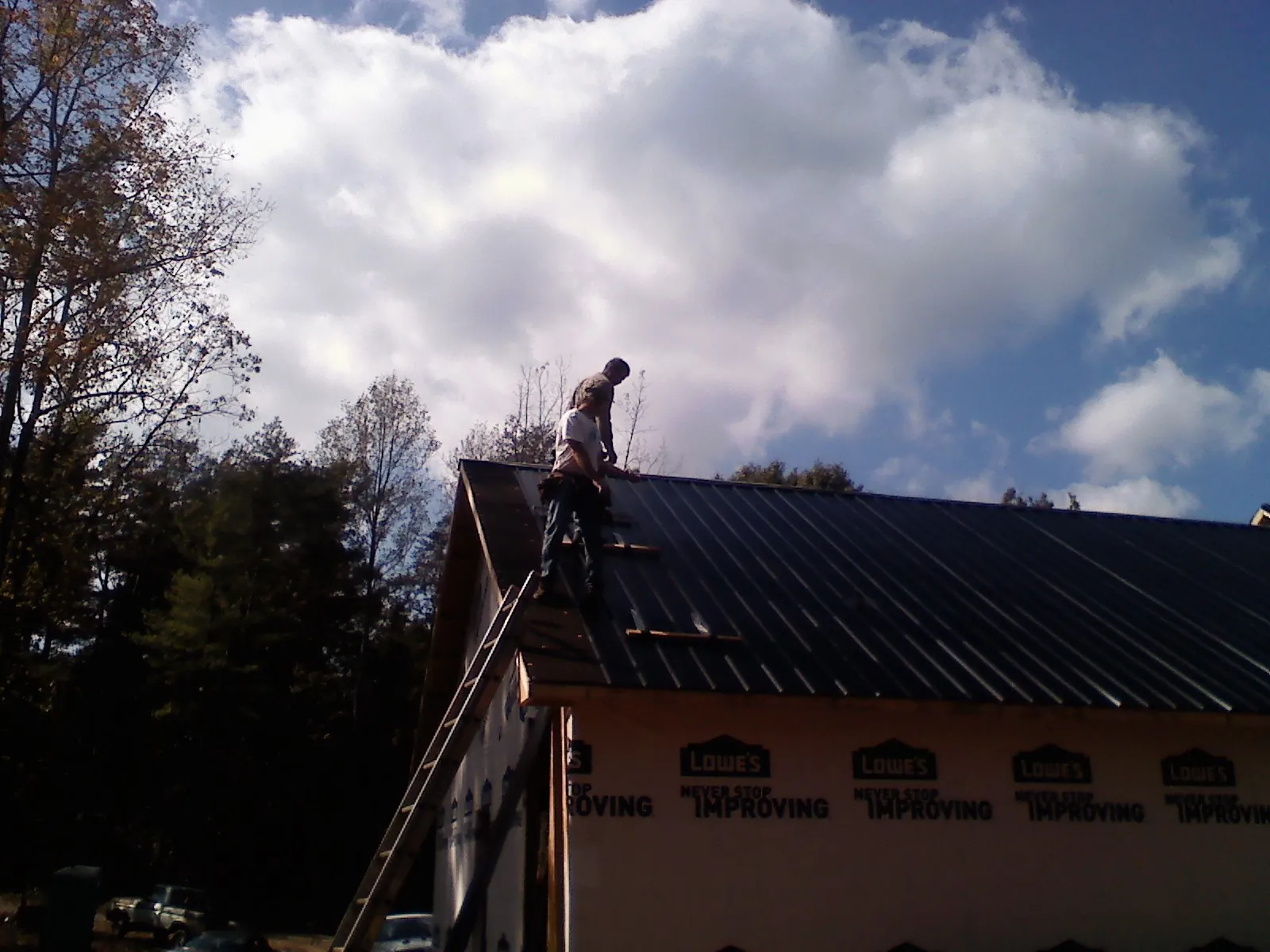 Roofer fastening dark metal panels high against a cloudy sky, from a Roof Inspection job in Cobalt